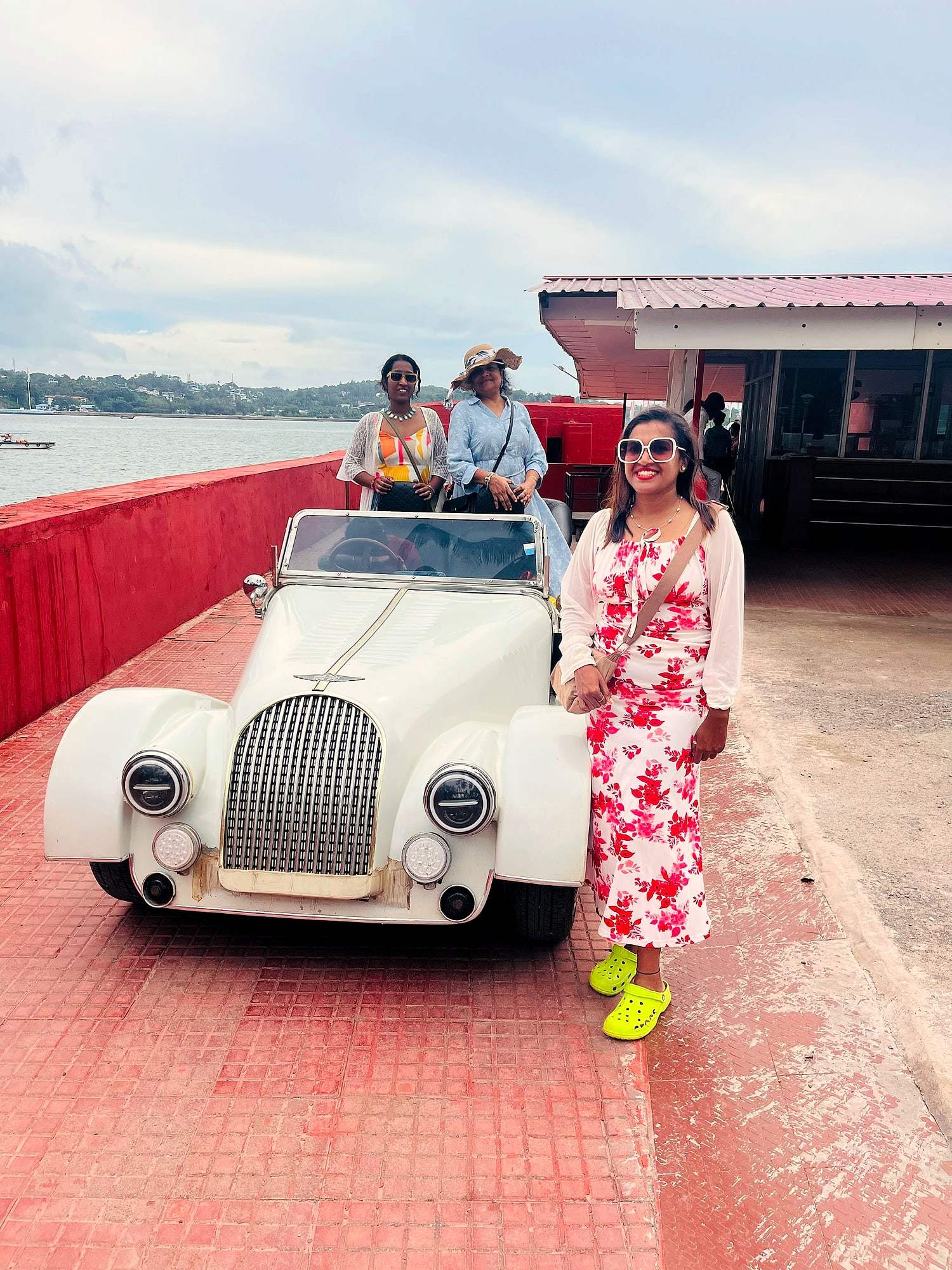 A traveller beside a vintage open-top car on a ferry deck