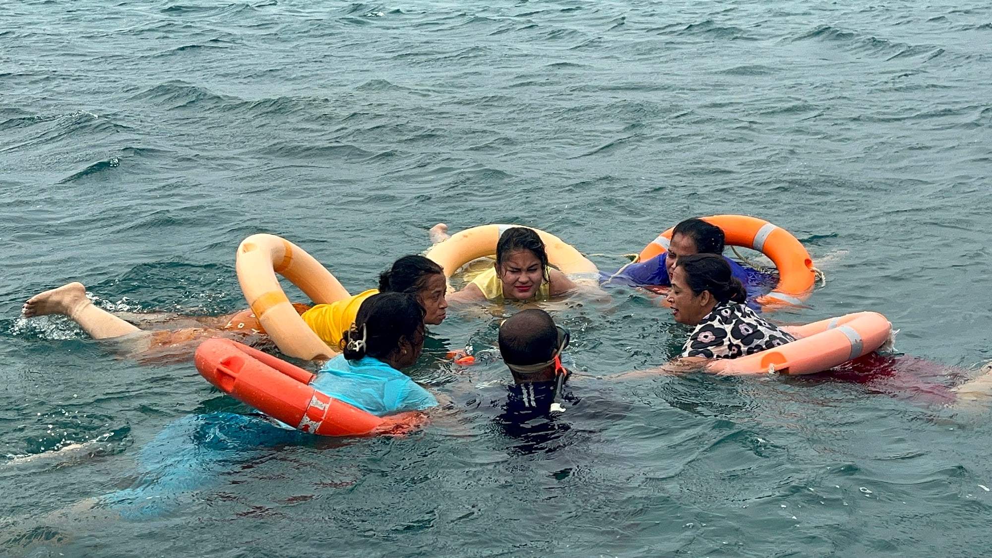 Travellers floating in turquoise water with orange life rings