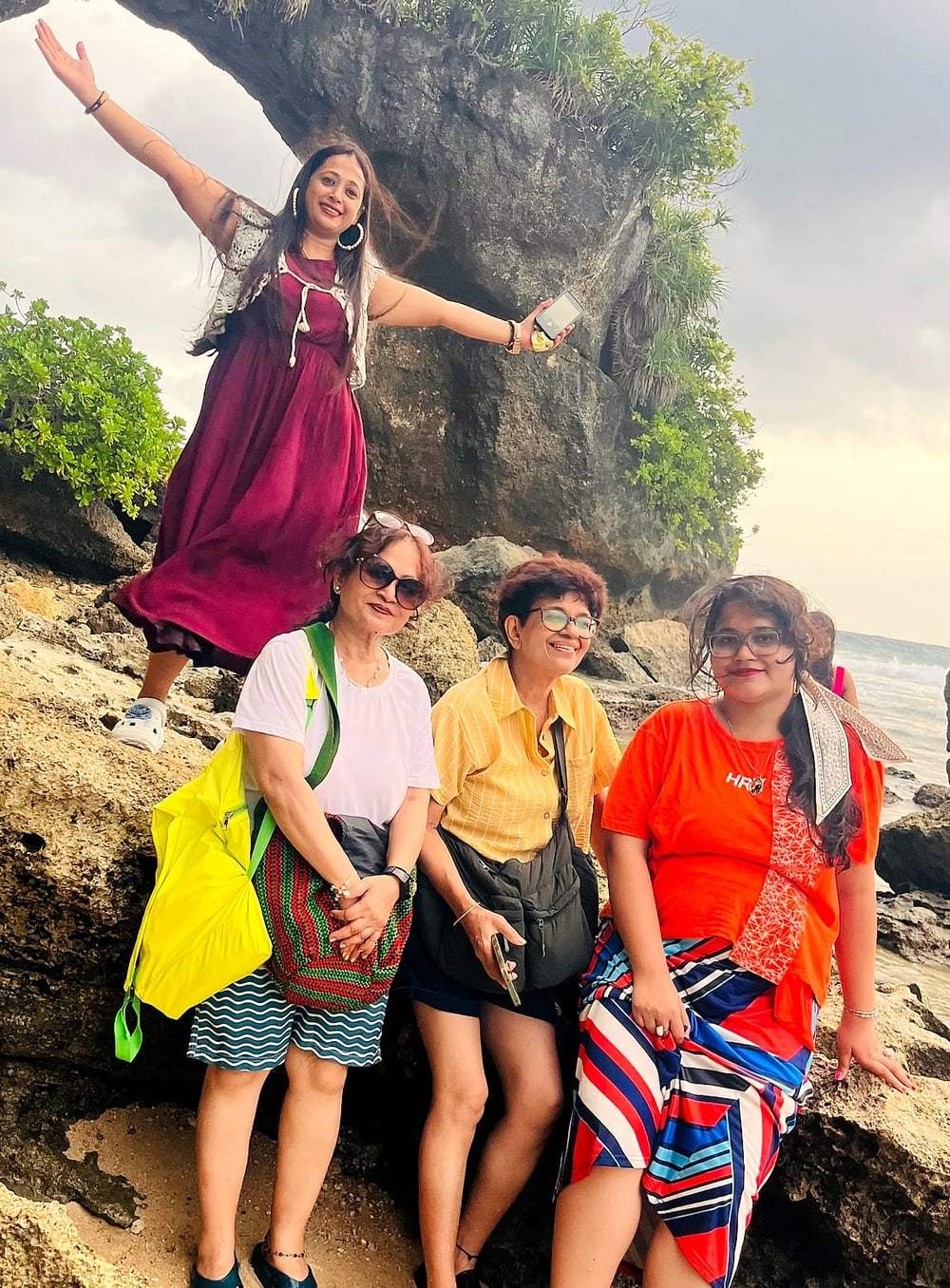 A traveller leaping with arms outstretched above friends on the rocks of an Andaman beach