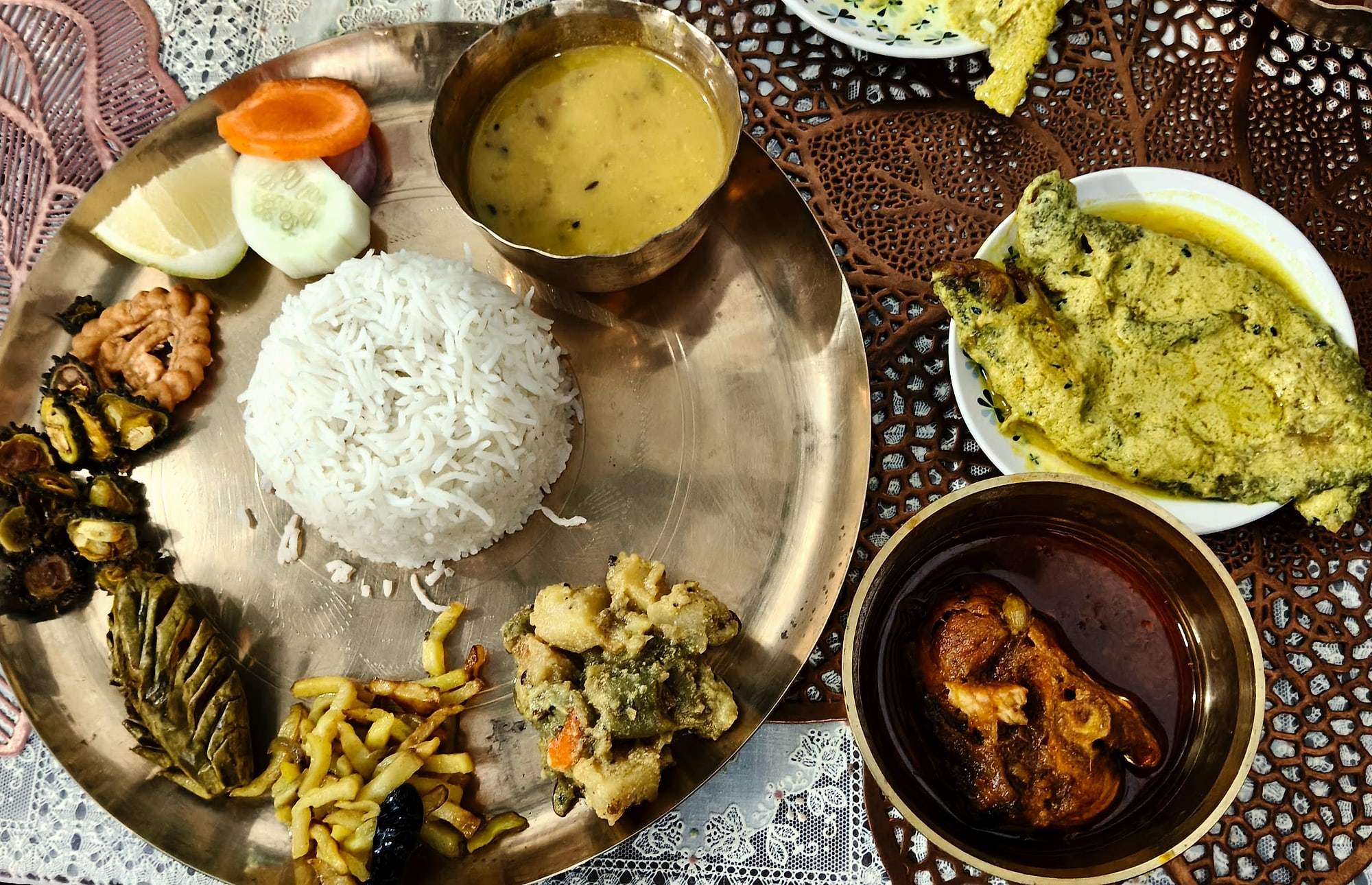 Fish curry, dal and fries arranged on a bronze thali